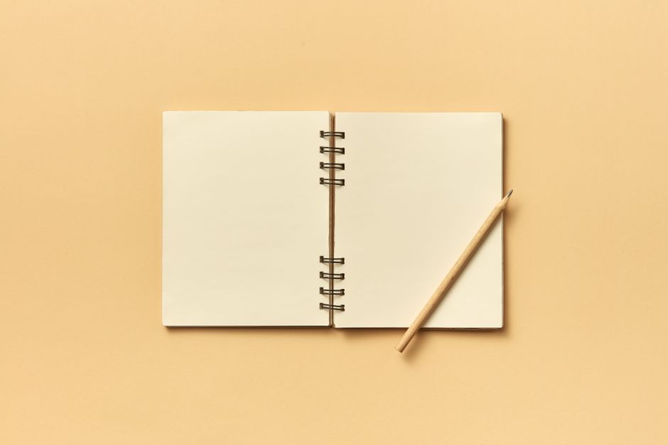 An open spiral notebook with a pencil on a neutral beige background, perfect for creative projects and planning.
