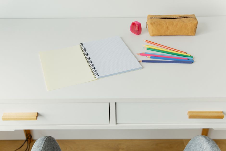 An organized workspace featuring a notebook with colored pencils and stationery on a white table.